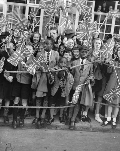 1200 children, from more than 100 schools, were among the great crowds which cheered Queen Mary when she opened the new £90,000 extension to Lambeth Town Hall, Brixton. Photo shows: black children waving flags as Queen Mary arrived. 14 October 1938